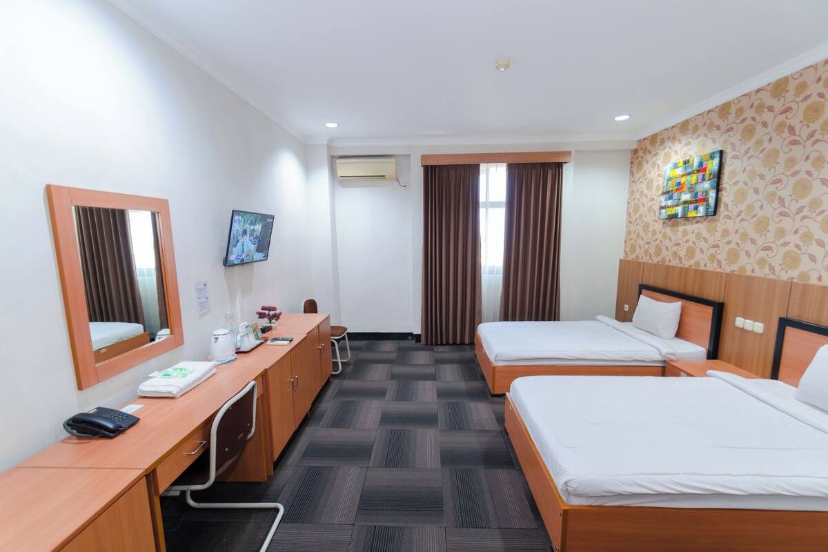 Une chambre d’hôtel avec deux lits, un bureau avec un téléphone, une chaise, une télévision et un appareil de climatisation.