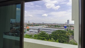 A cityscape through a window with buildings, trees, and a clear sky. - Graha Widya Bhakti at STIESIA Surabaya (Surabaya)