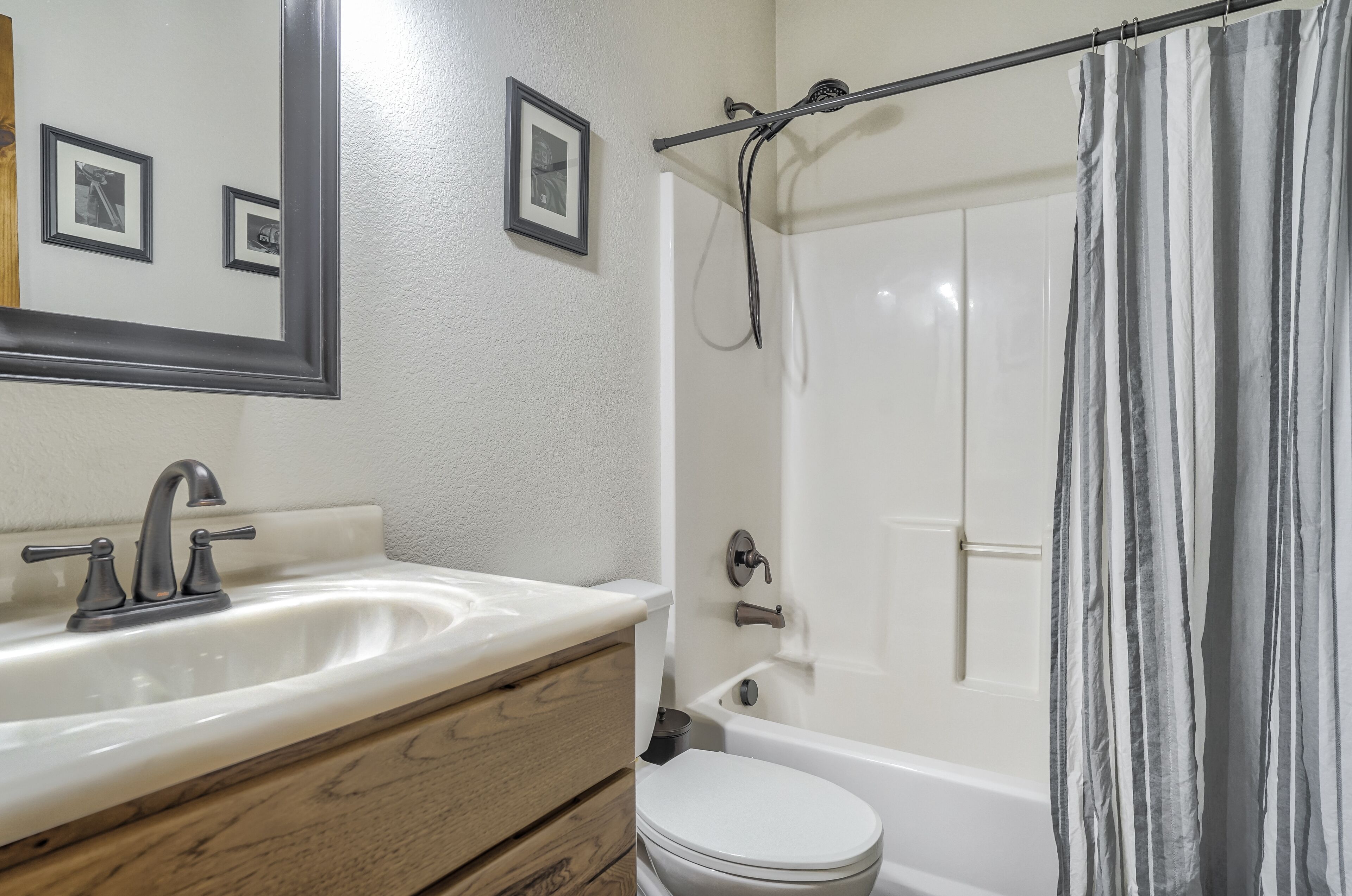 A bathroom with a white sink, wooden vanity, a toilet, and a bathtub with a shower curtain.