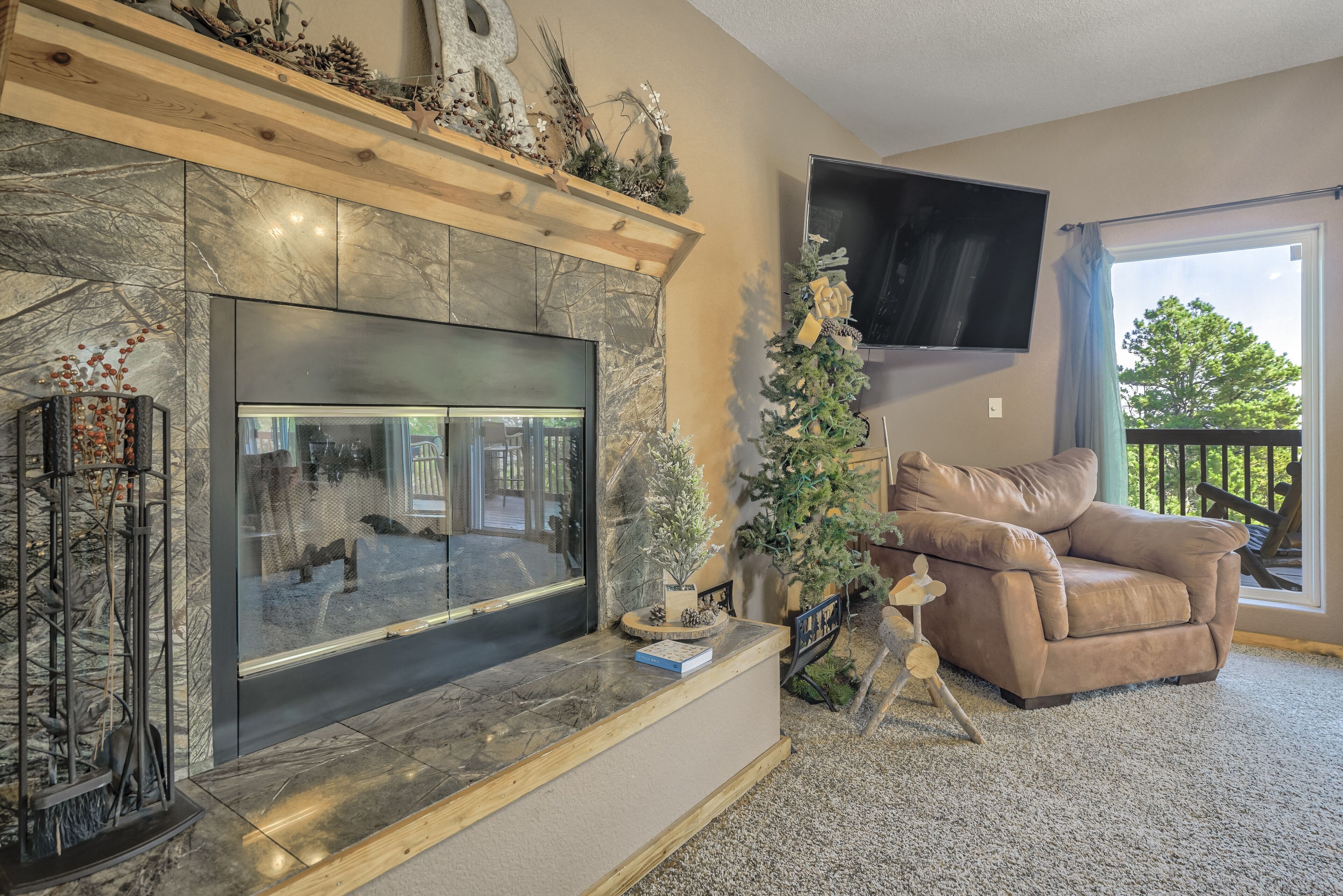 Una sala de estar con chimenea, televisor montado, árbol de Navidad y sofá de cuero.
