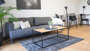 A modern living room with a grey sofa, a coffee table, a potted plant, and a large bull artwork on the wall. - Charming Homes - Studio 25 (Weyhausen)