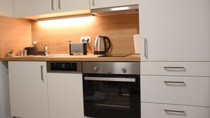 A modern kitchen with white cabinets, a stainless steel dishwasher, an oven, and a wooden countertop. - Charming Homes - Studio 25 (Weyhausen)