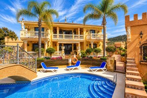 Un grand bâtiment doté d’une piscine, de palmiers et d’un balcon avec des chaises longues.