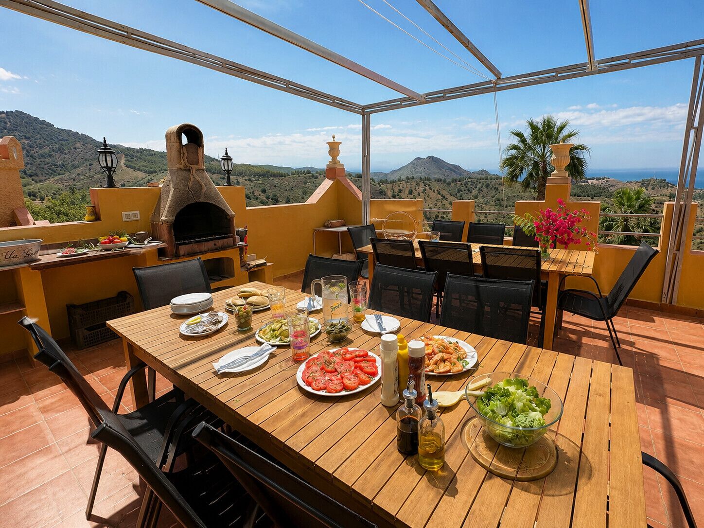 Un espace extérieur aménagé pour les repas, avec vue sur les montagnes, un four à pizza et une table dressée.