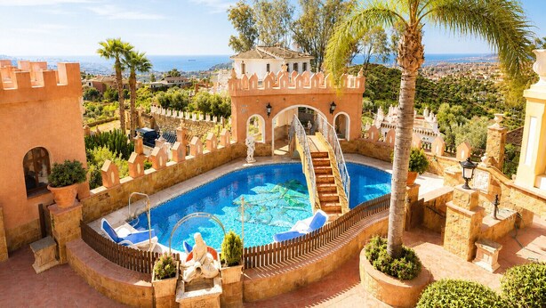 Una piscina con una estructura similar a un castillo, una escalera que da a la piscina y vistas de la ciudad al fondo.