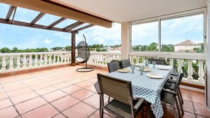 A balcony with a table set for dining, a hanging chair, and a view of the sea and buildings. - Tranquil Paradise, Private Pool - only 200m to beach! (El Perelló)