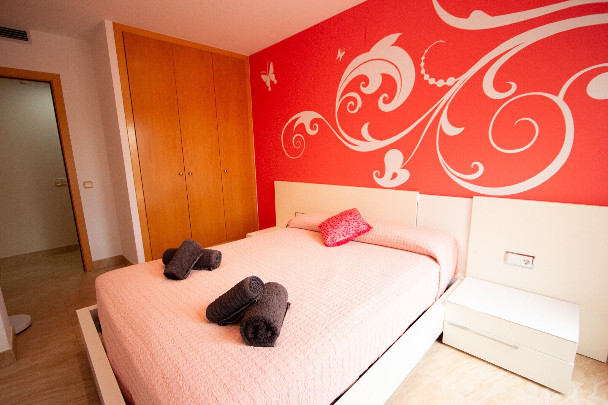 Ein Hotelzimmer mit einem Bett, einem Holzschrank, einem weißen Nachttisch und einer roten Wand mit weißen Verzierungen.