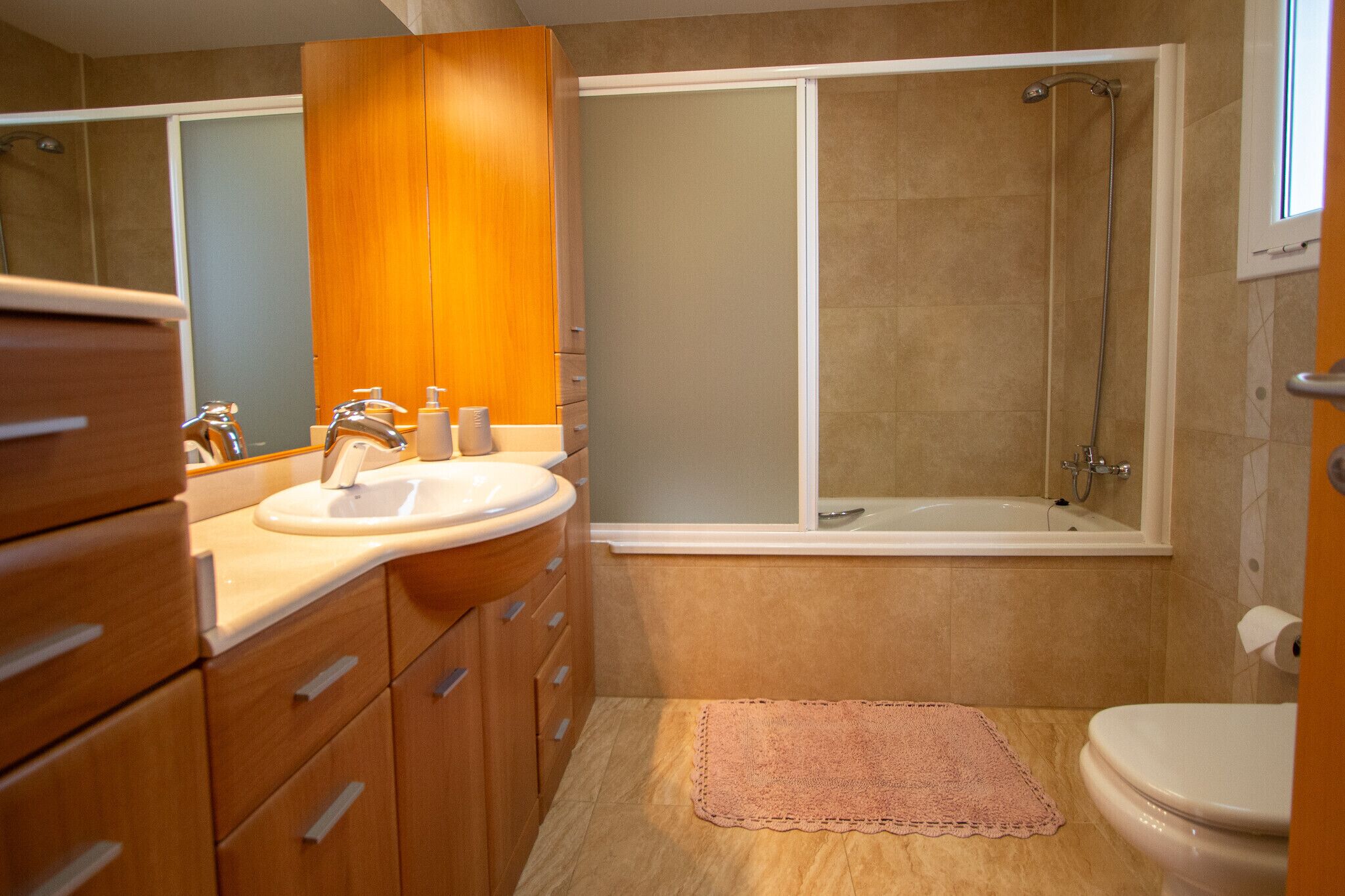A modern bathroom with a wooden vanity, a sink, a toilet, and a walk-in shower.