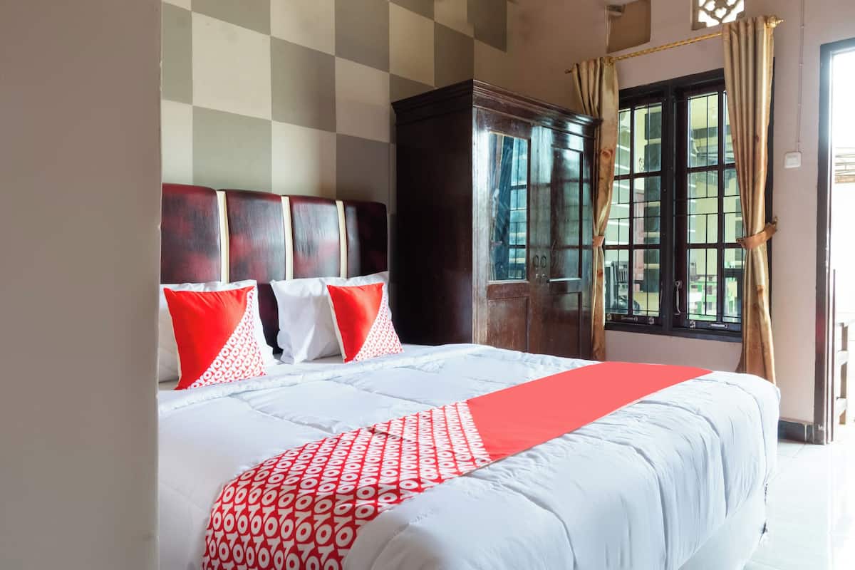 A hotel room with a large bed, a wooden headboard, and a window with curtains.