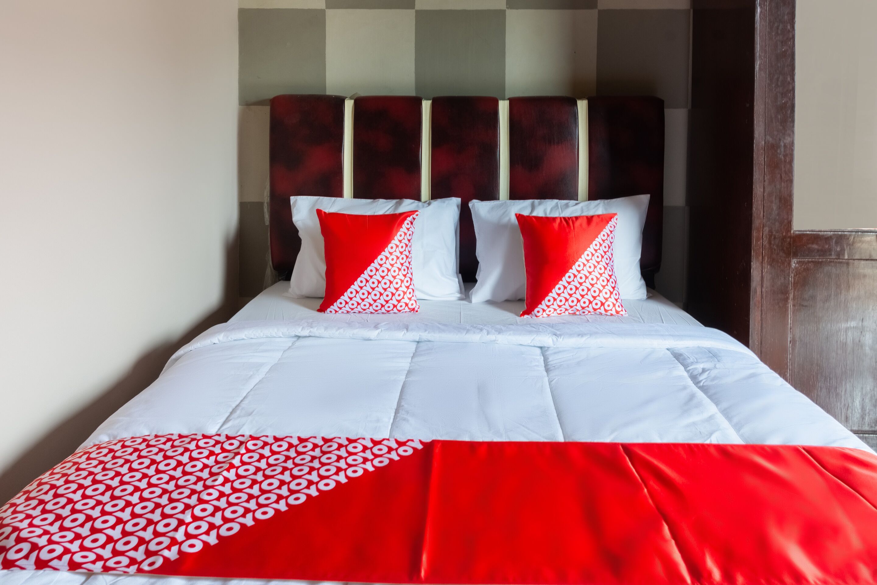 A bed with white and red bedding, a patterned pillow, and a headboard with a geometric design.