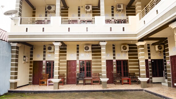Un edificio de dos pisos con balcón, varias puertas y mobiliario para exterior.