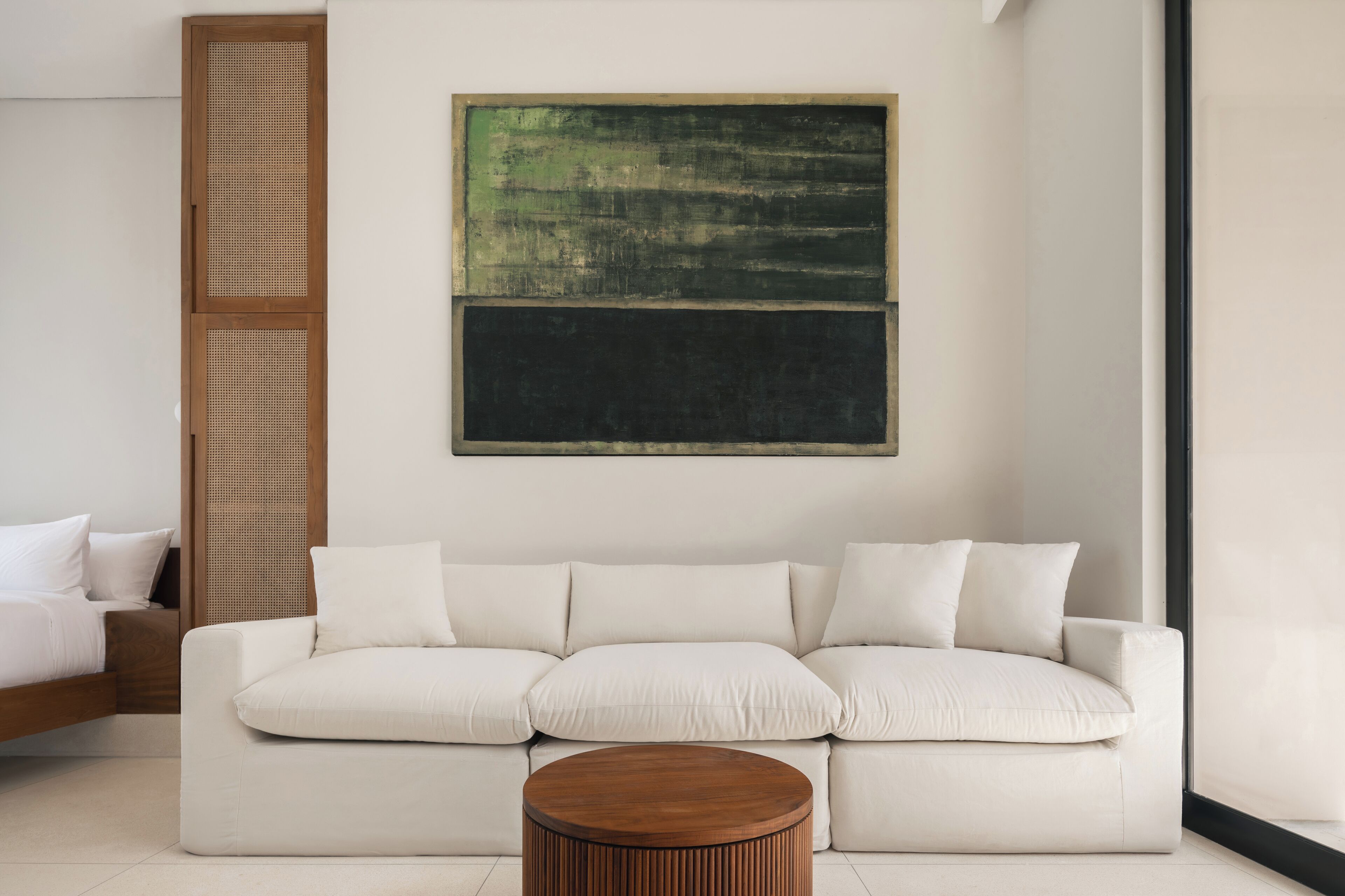Un salon moderne avec un canapé blanc, une table basse en bois et un grand tableau abstrait accroché au mur.