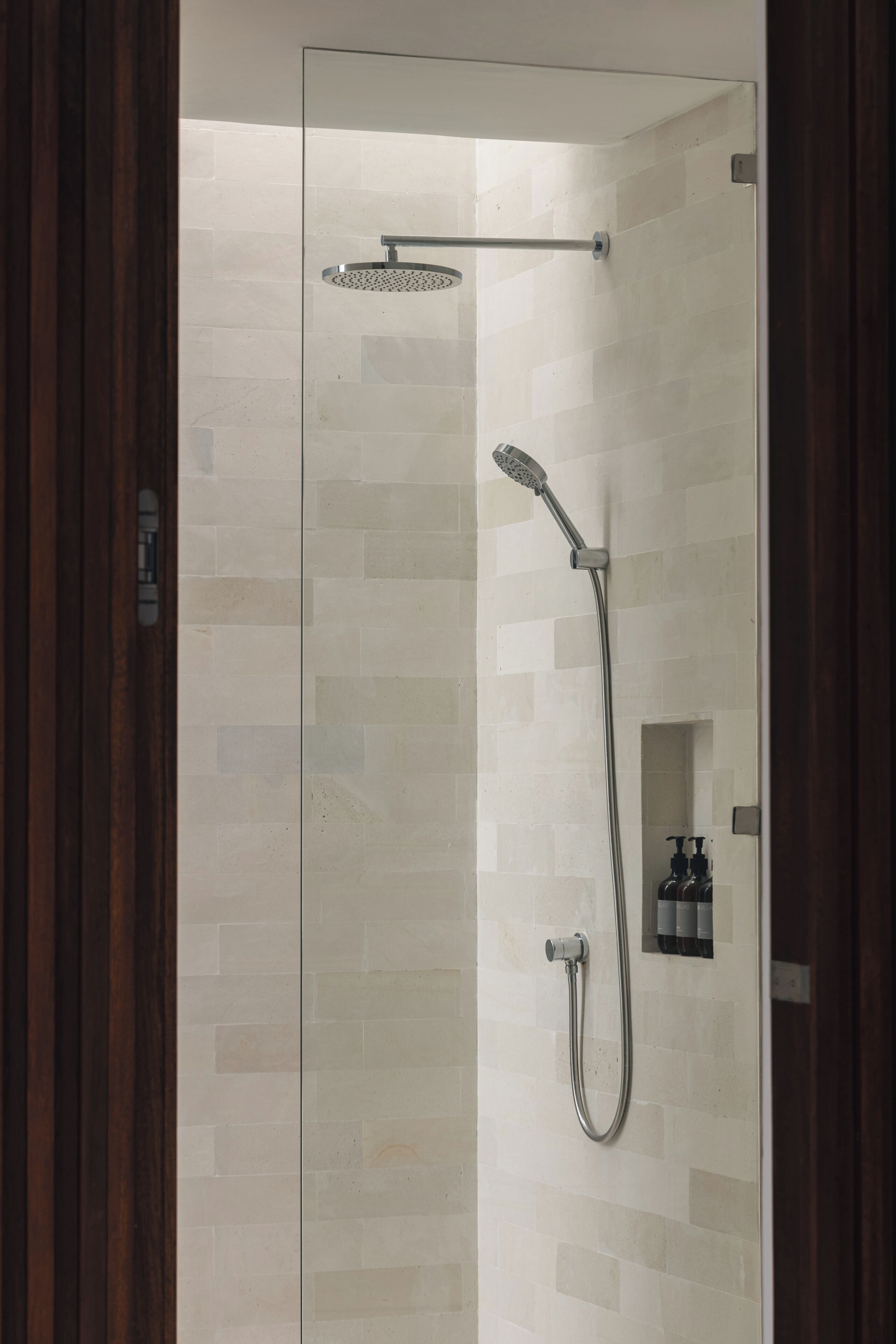 A glass-enclosed shower with a handheld showerhead and a wall-mounted faucet.