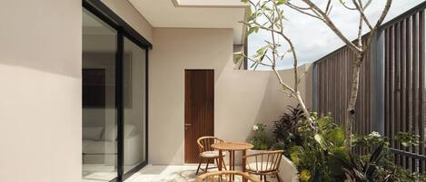 A modern outdoor patio with a wooden table and chairs, a small garden area with plants, and a view of the sky.