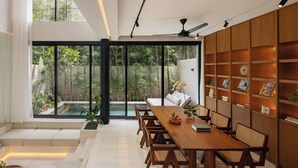 Uma sala de jantar moderna com uma mesa e cadeiras de madeira, uma estante e vista para um jardim através de grandes janelas.
