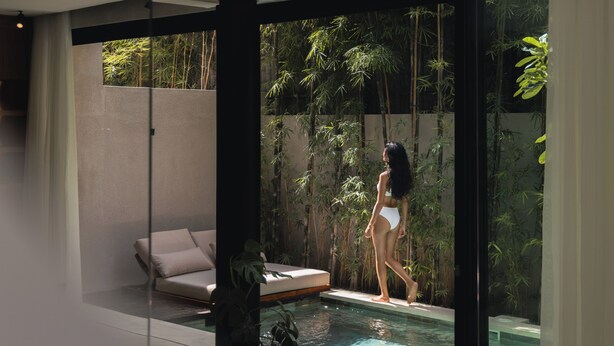 Uma área interna de piscina moderna com parede de vidro, um sofá e plantas de bambu.