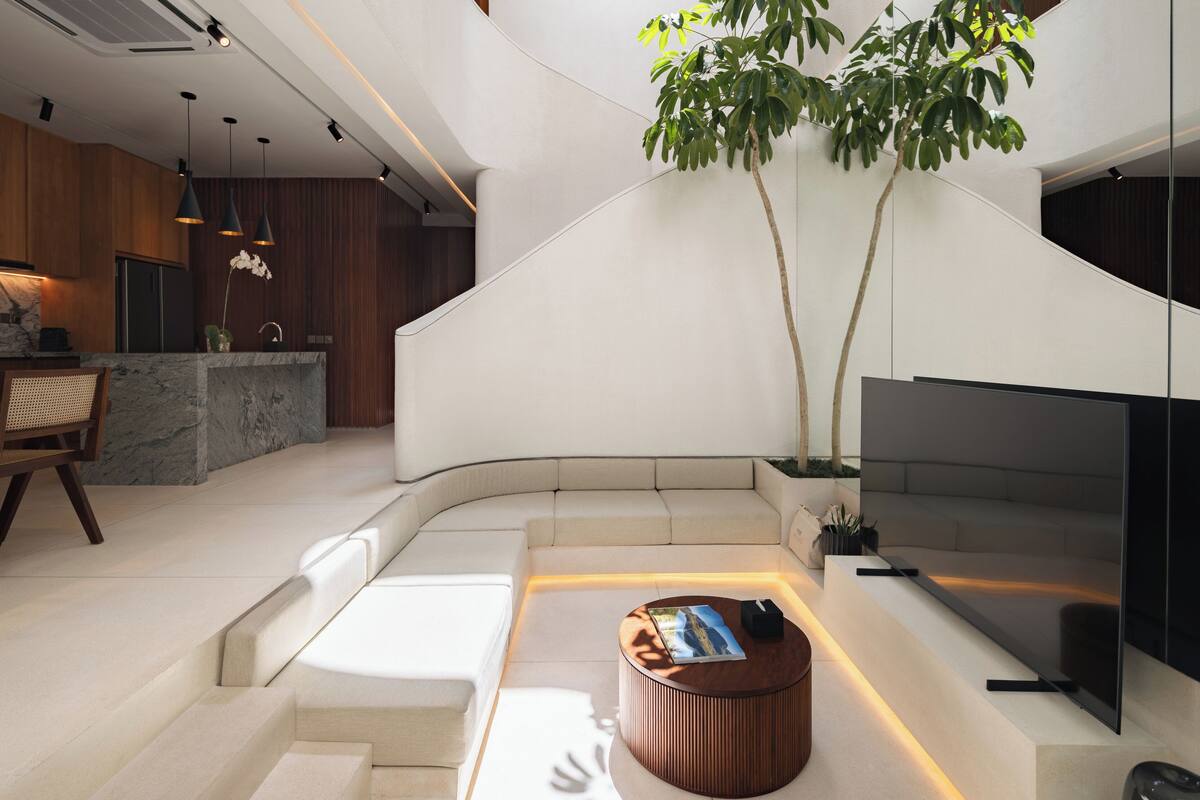 Un interior moderno con una escalera curva, un área de estar central, un televisor de pantalla plana y un tragaluz.