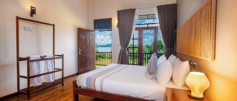 A bedroom with a wooden bed, a nightstand with a lamp, a wardrobe, and a view of the outdoors.