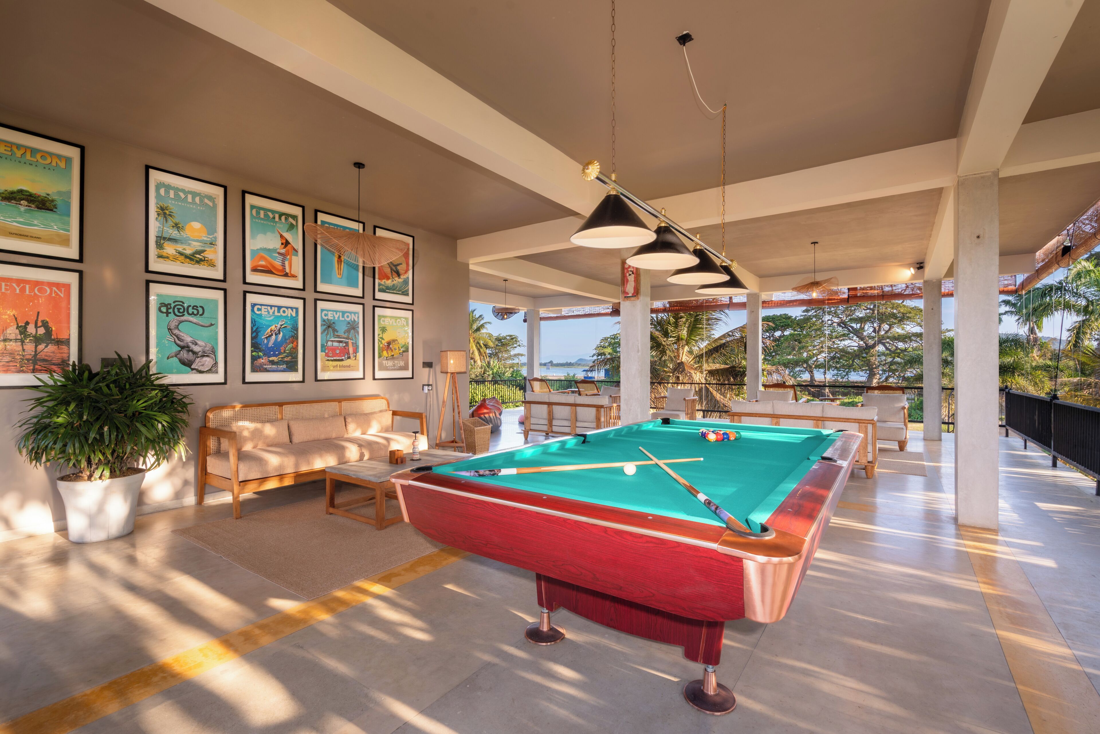 A pool table in a well-lit room with framed pictures on the wall, a sofa, and a potted plant.