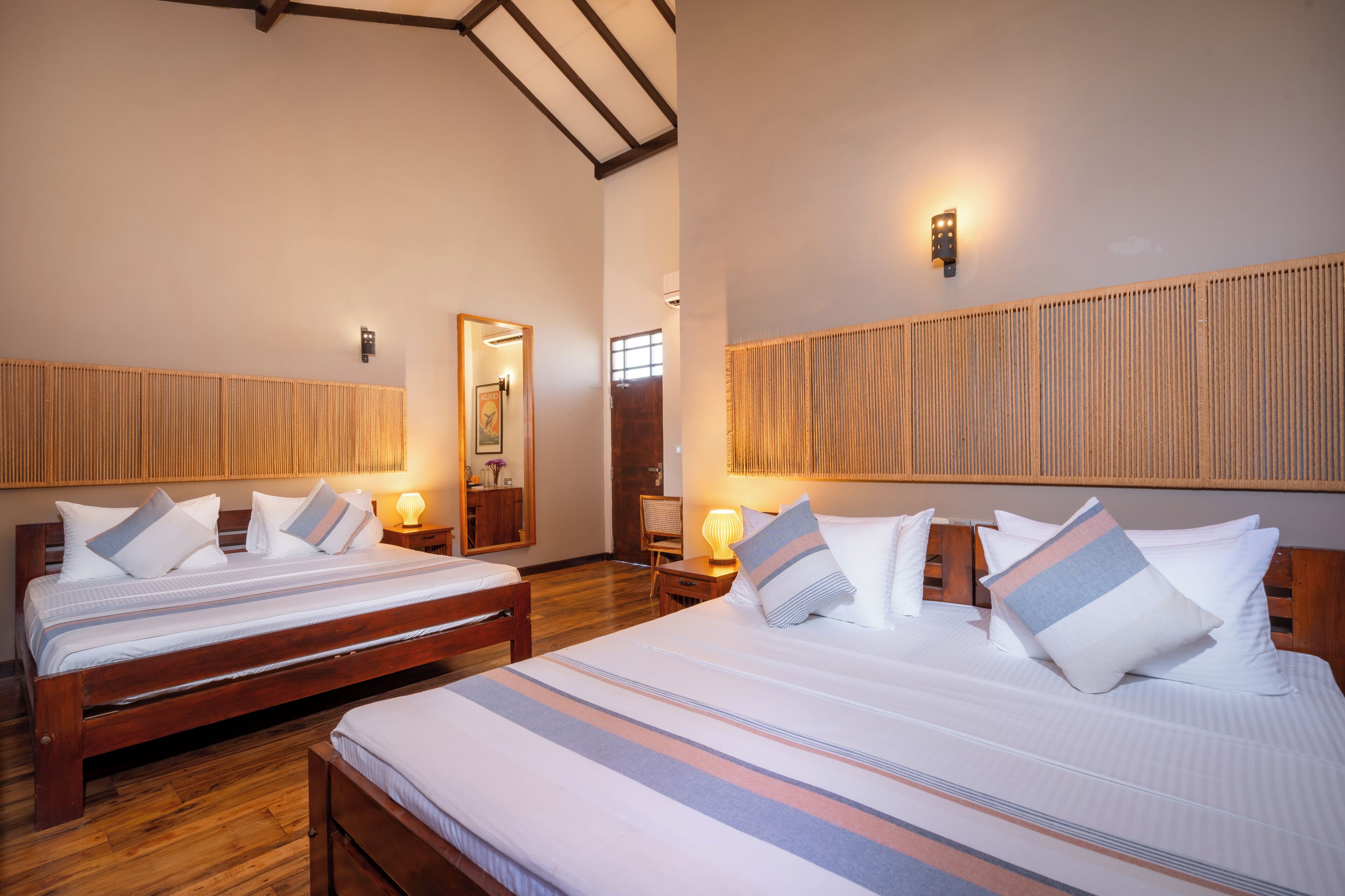 Two double beds with striped bedding, wooden headboards, bedside lamps, and a wooden floor.