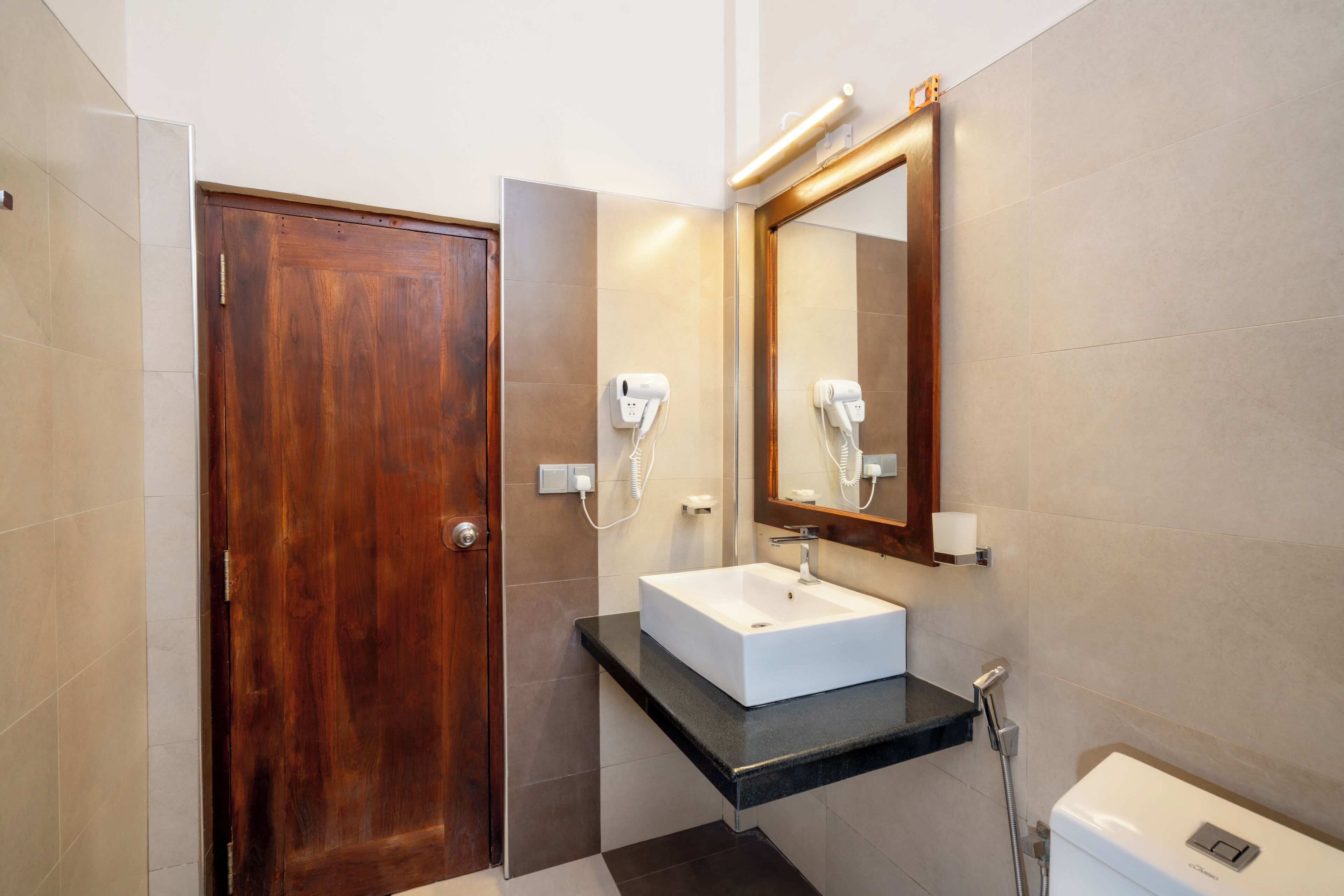 A bathroom with a wooden door, a white sink, a mirror, and a toilet.