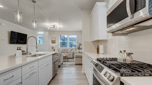 A modern kitchen with white cabinetry, a built-in stove, and a large window. - Rio Grande (Colorado Springs)