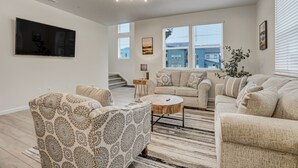 A spacious living room with a large flat-screen TV mounted on the wall, a sofa set, a coffee table, and a staircase leading to an upper floor. - Rio Grande (Colorado Springs)
