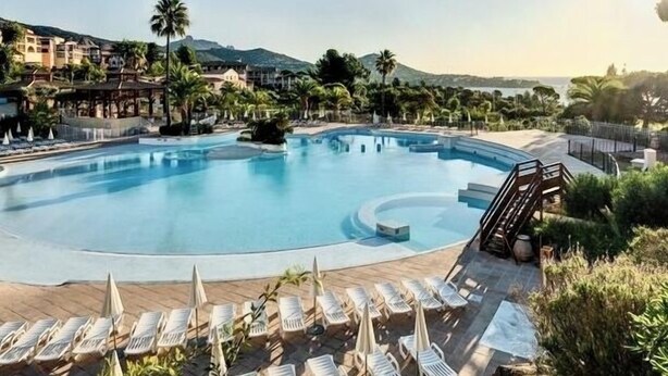 A swimming pool with lounge chairs and umbrellas, surrounded by palm trees and buildings. - The Garden by the Sea (Saint-Raphaël)