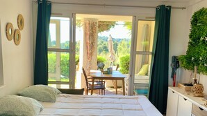 Ein Zimmer mit einem Bett, einem Tisch und Blick auf Grünfläche.