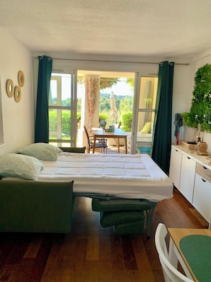 A room with a bed, a table, and a view of greenery outside. - The Garden by the Sea (Saint-Raphaël)