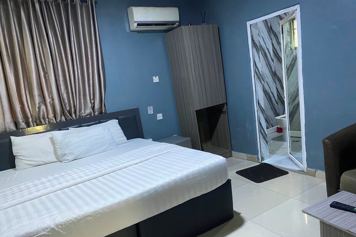 A modern bedroom with a large bed, a wardrobe, a mirror, and a small table.