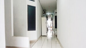 A corridor with white walls and tiled flooring, leading to a room with a window and a door. - Hotel O Bintang Residence (Jakarta)
