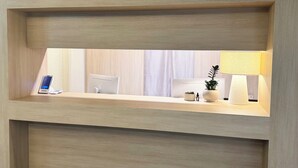 Mostrador de recepción de hotel con una computadora, un teléfono, una lámpara y una planta pequeña.