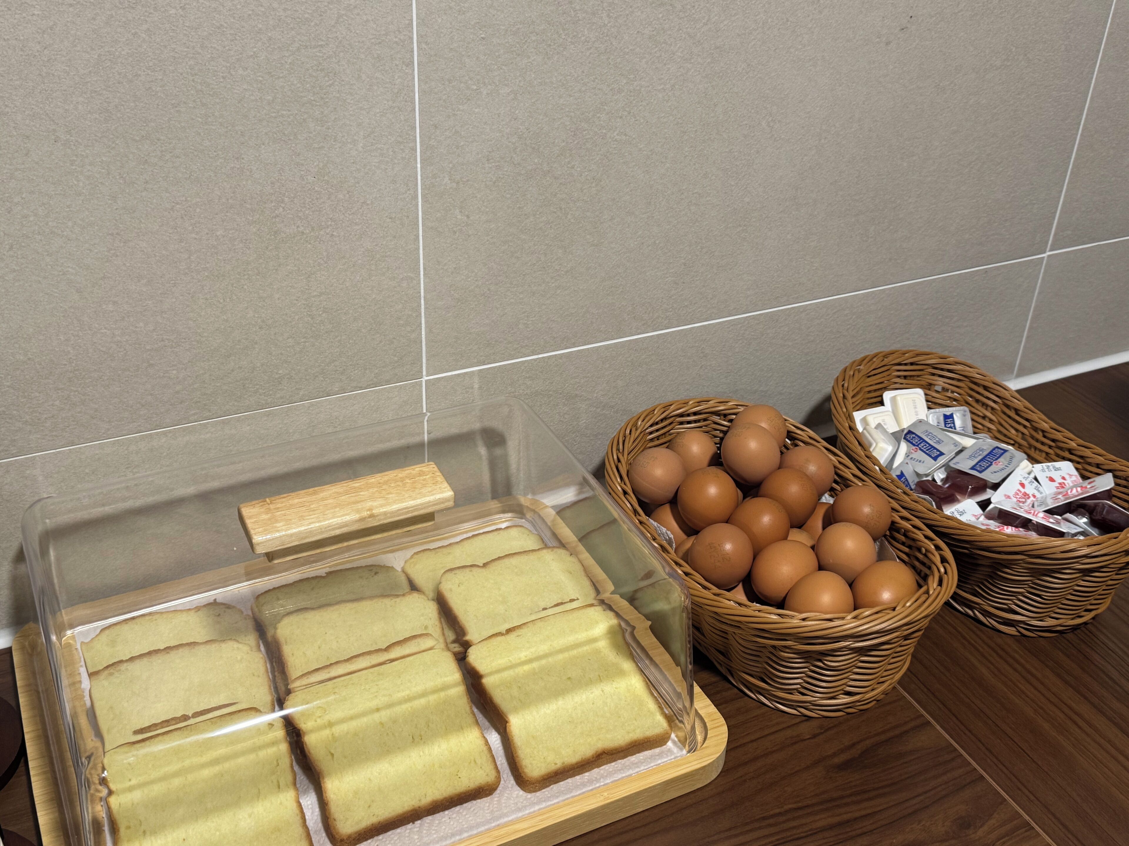 Una encimera de cocina con un recipiente de plástico transparente lleno de rebanadas de pastel, una cesta de mimbre con huevos y otra cesta de mimbre con productos envasados.