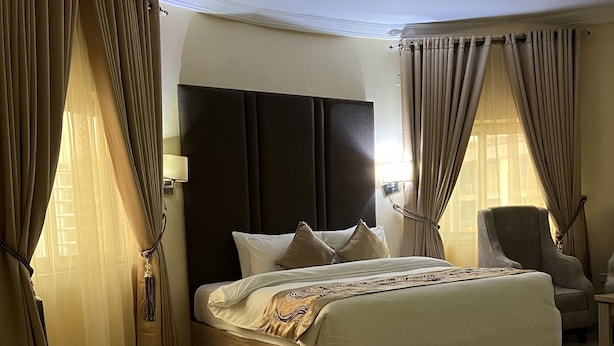 A hotel room with a large bed, a dark headboard, and curtains on the windows. - JVM Hotel (Karu)
