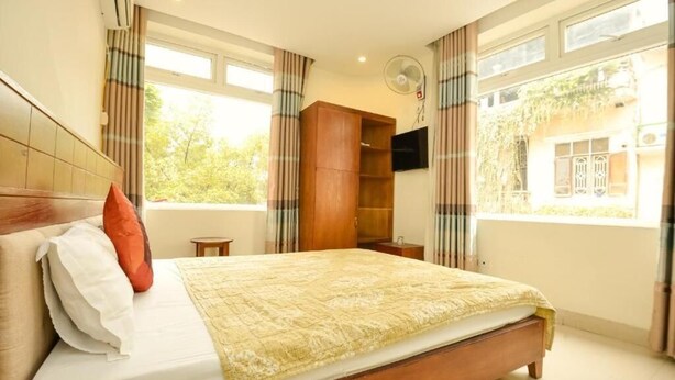 A bedroom with a bed, a wooden wardrobe, a TV mounted on the wall, and a window with curtains. - Ha Noi Vang Hotel by Bay Luxury (Hanoi)
