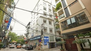 A hotel with a signboard, parked cars, and a narrow street with buildings on either side. - Ha Noi Vang Hotel by Bay Luxury (Hanoi)