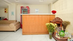 A reception area with a wooden counter, a Coca-Cola refrigerator, a sofa, and a small altar with flowers and offerings. - Ha Noi Vang Hotel by Bay Luxury (Hanoi)