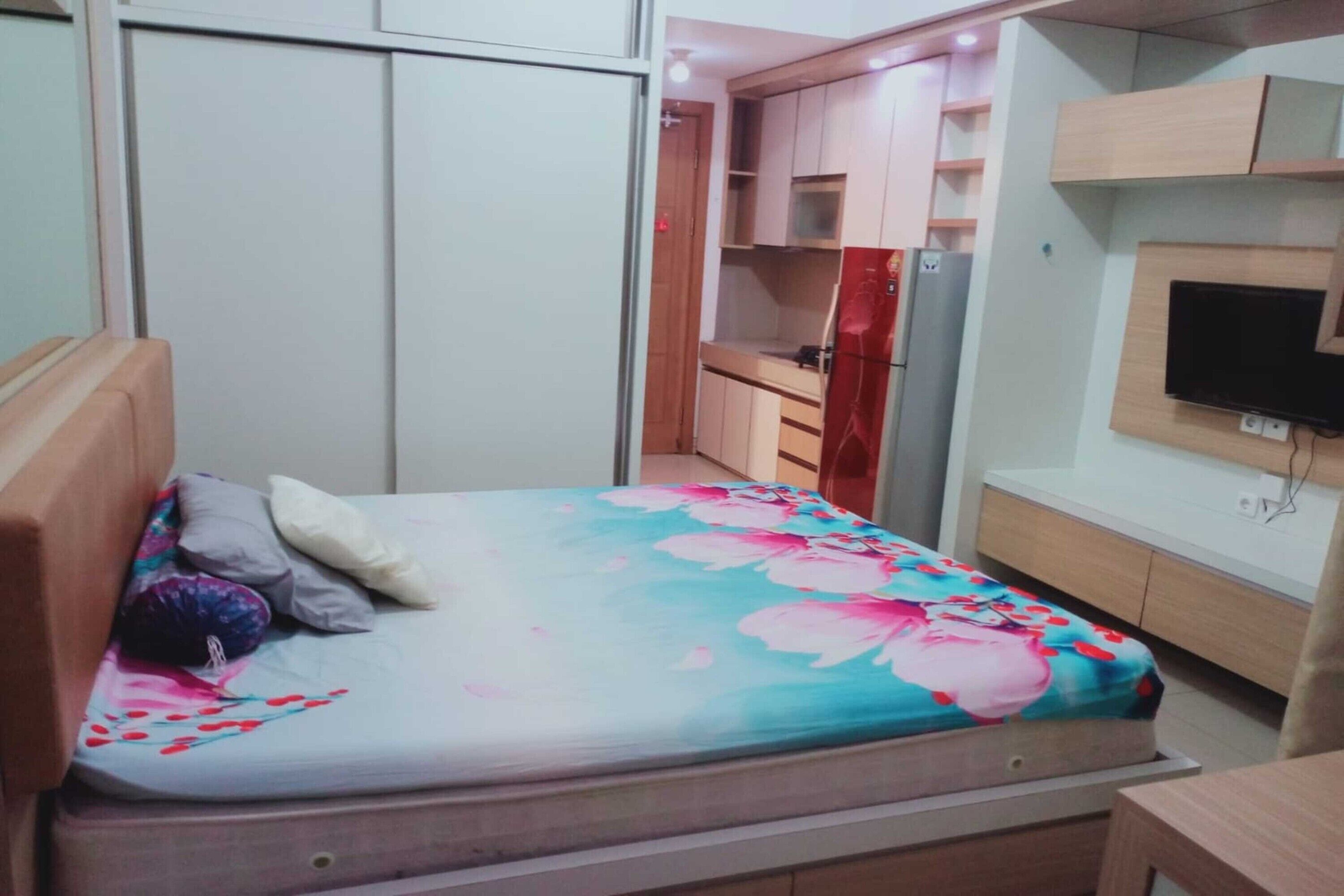 A bedroom with a bed, a TV mounted on the wall, and a kitchenette area.