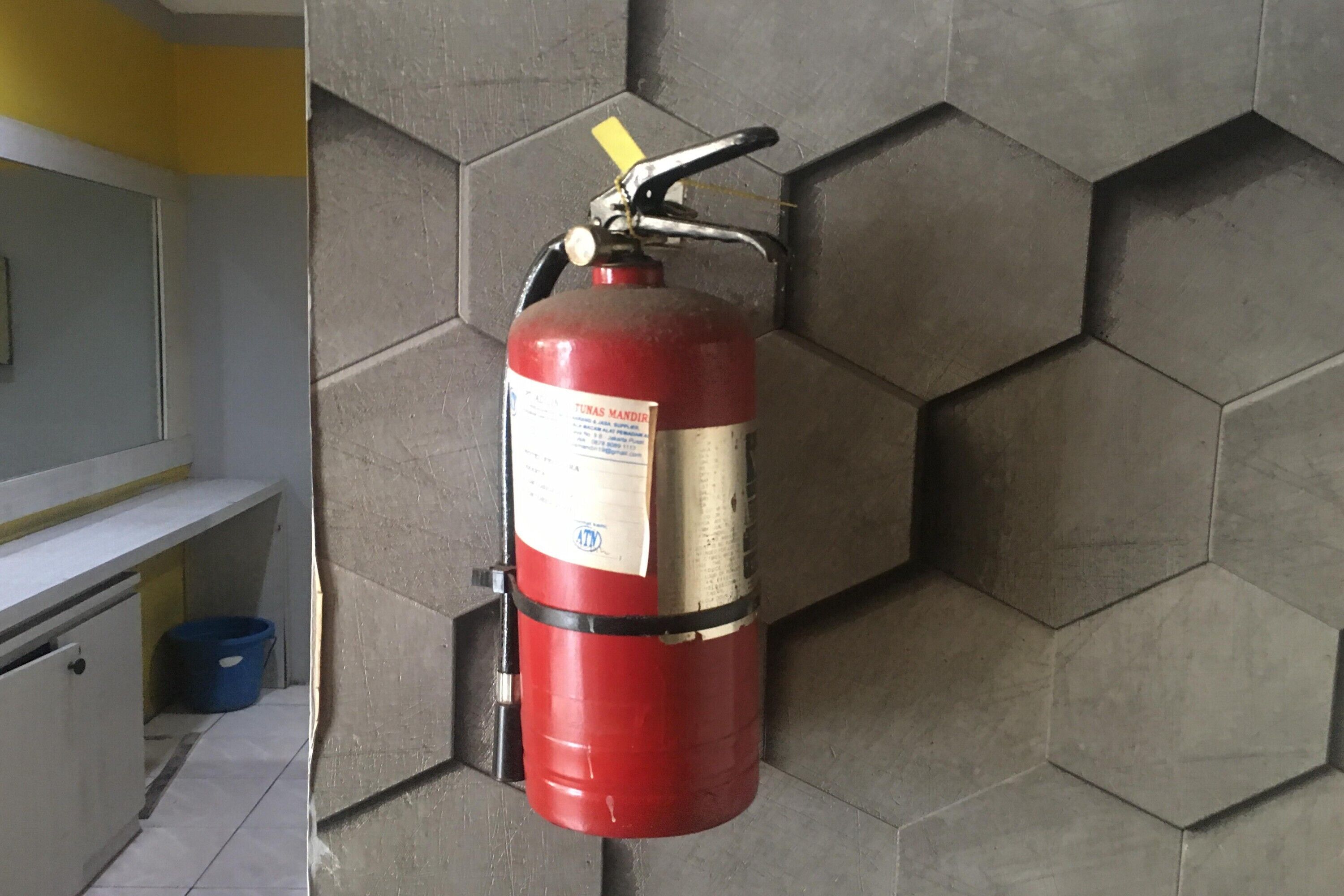 Un extintor rojo montado en una pared de azulejos hexagonales en una habitación con un mostrador blanco y un cubo azul.