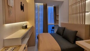 A modern hotel room with a bed, bedside table, and a view of the cityscape through large windows. - OYO 93543 Belmount Residence Near SILOAM CLINIC MERUYA (Jakarta)