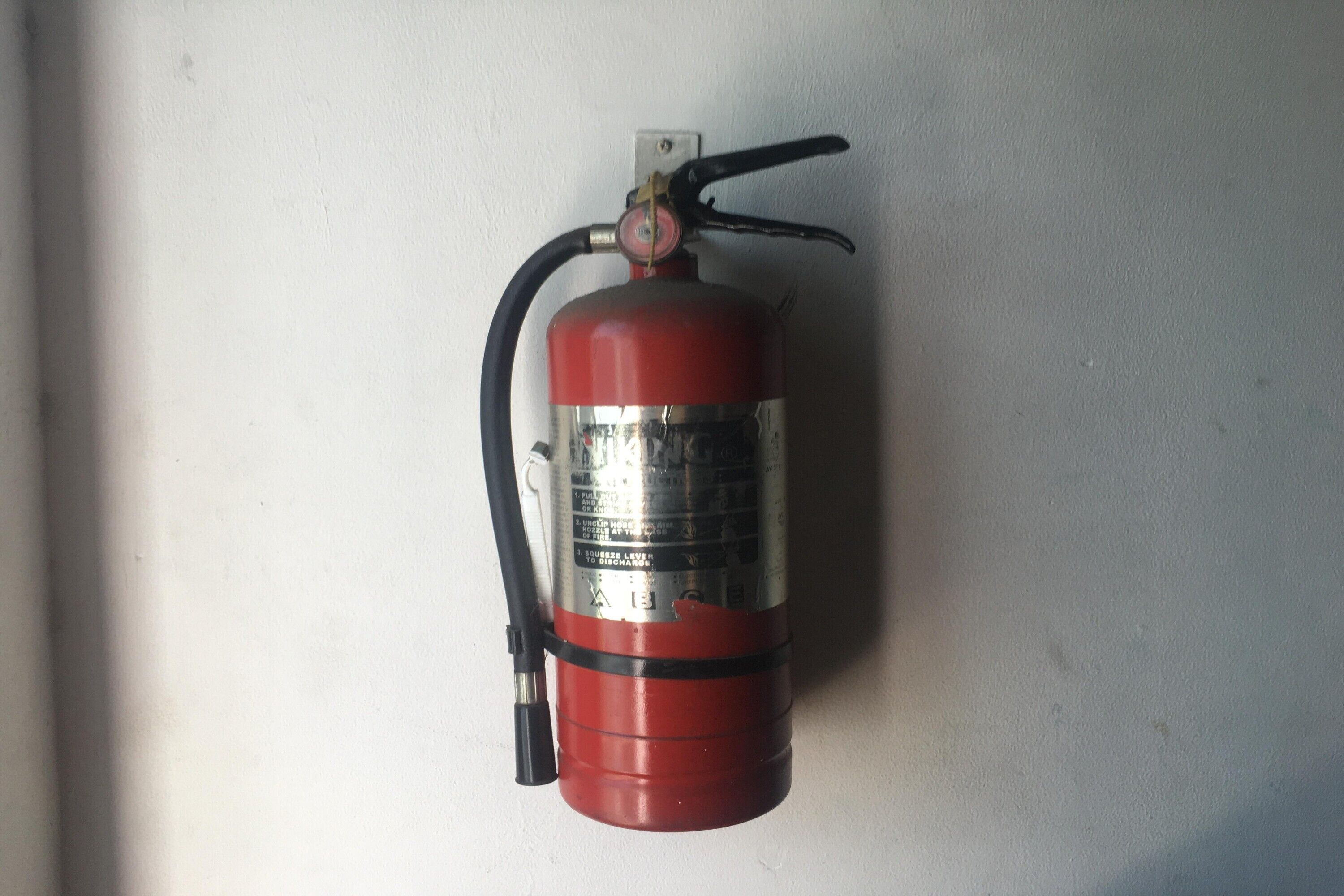 Un extincteur rouge fixé sur un mur blanc.