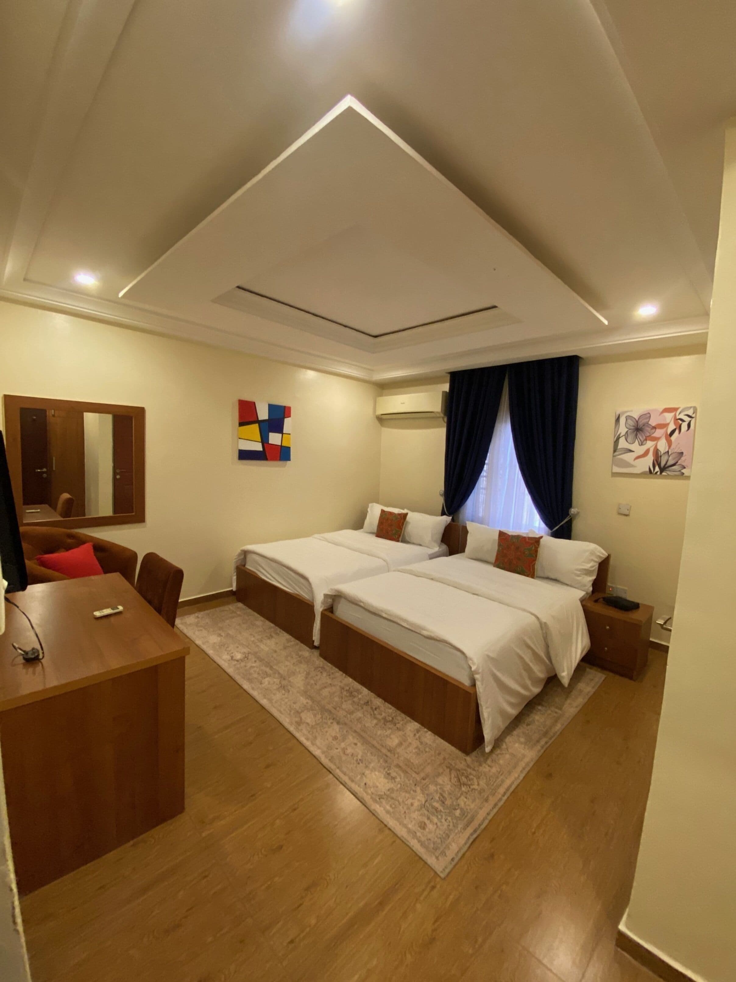 A hotel room with two beds, a desk, and a mirror.