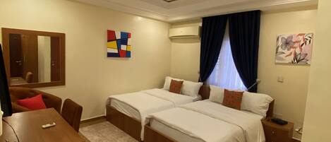 A hotel room with two beds, a desk, and a mirror.