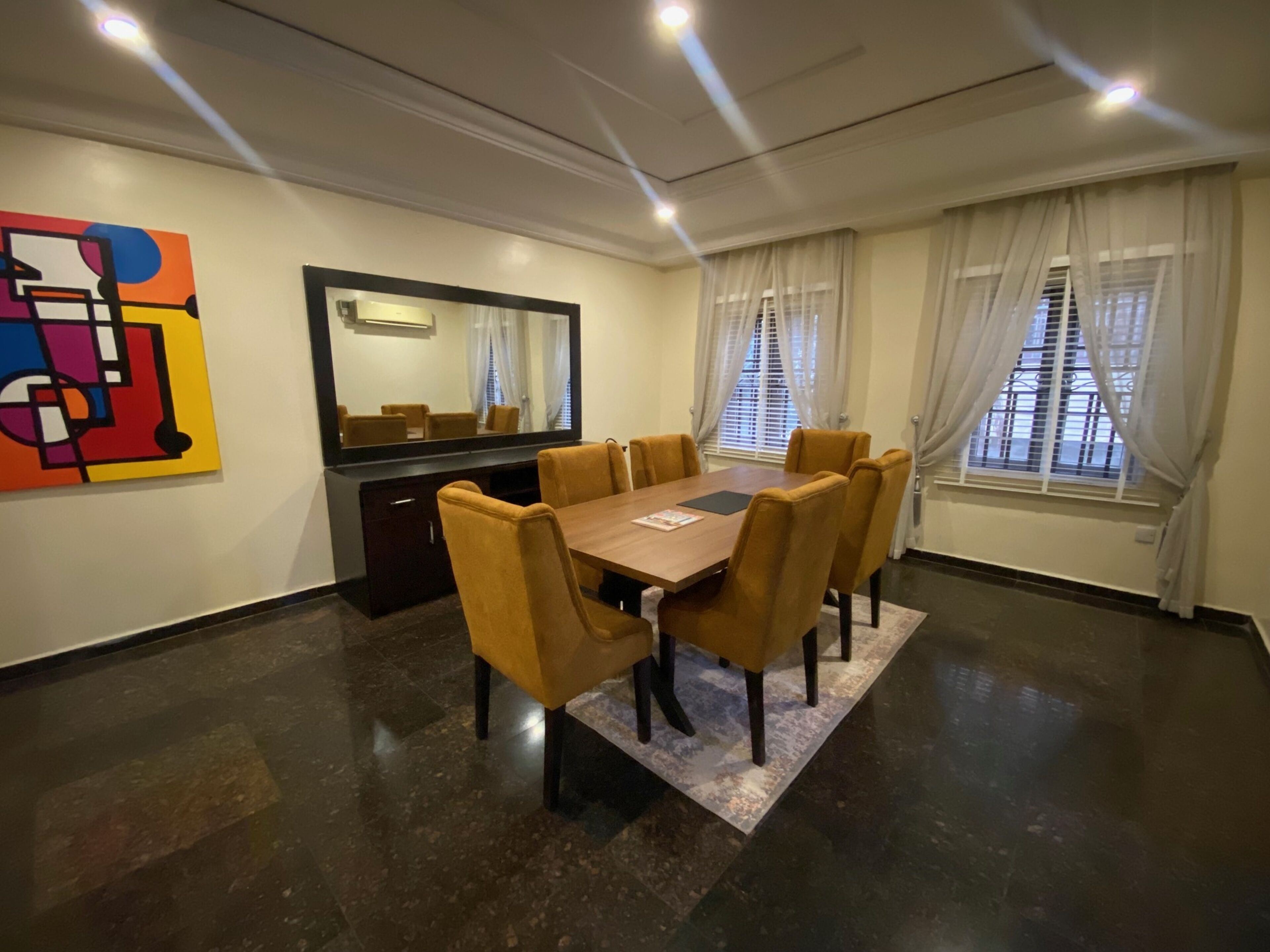 Une salle de conférence avec une grande table, des chaises, un miroir et un tableau abstrait aux couleurs vives accroché au mur.