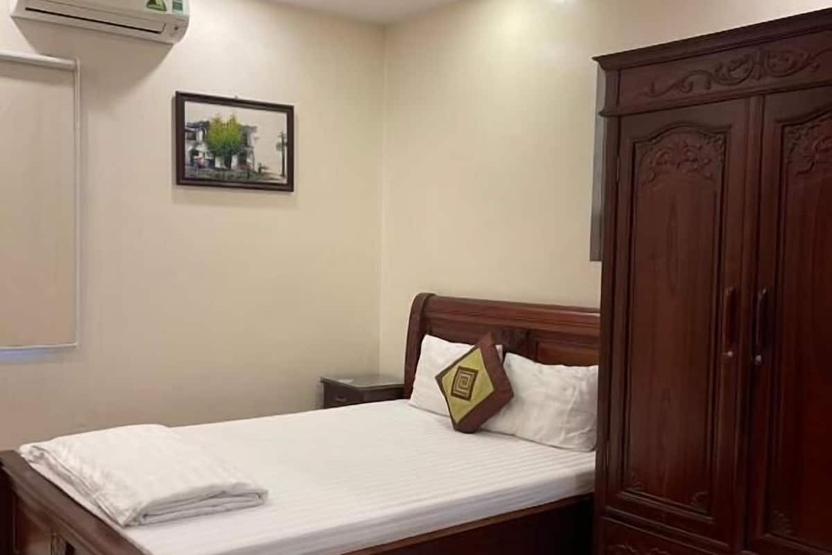 Un lit bien fait, avec des draps blancs, une tête de lit en bois et un seul coussin décoratif.