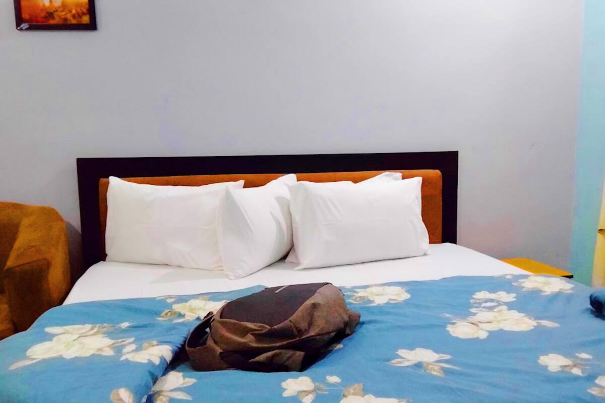 A bed with a floral bedspread, white pillows, and a brown bag on it.