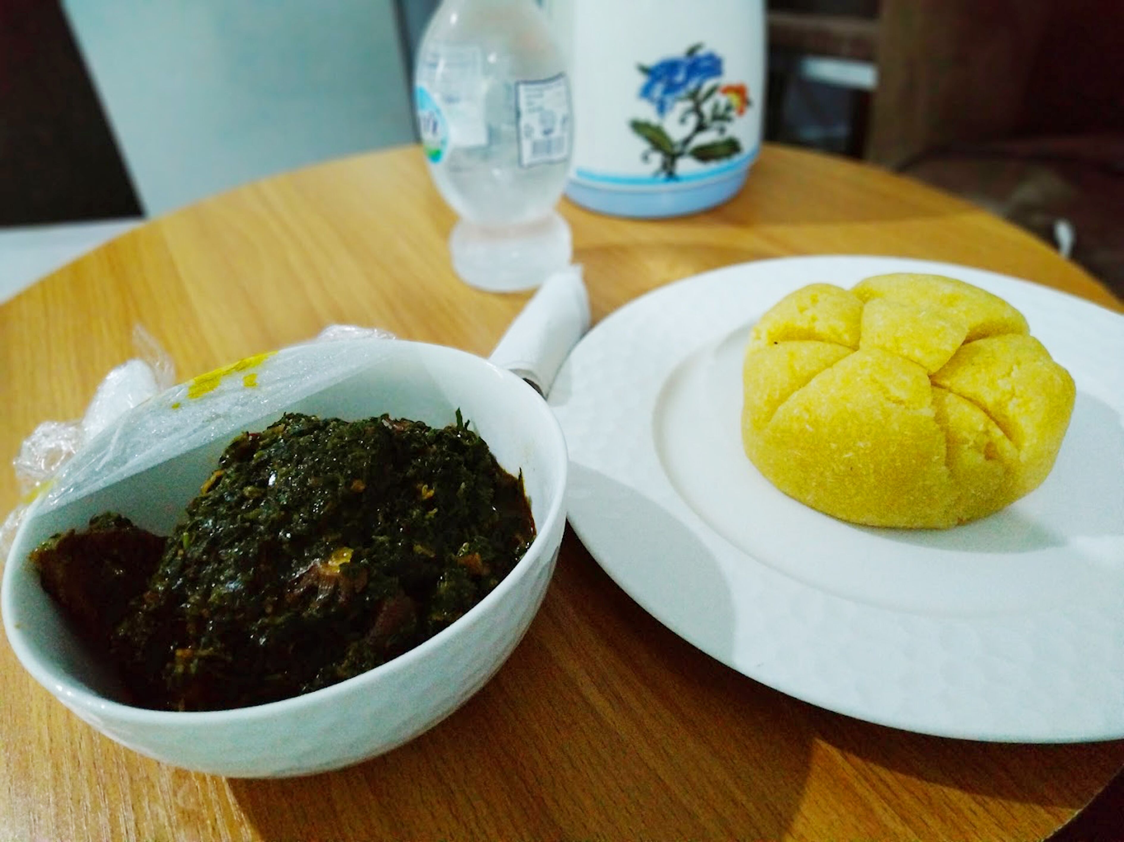A plate with a yellow food item and a bowl of dark green leafy dish.