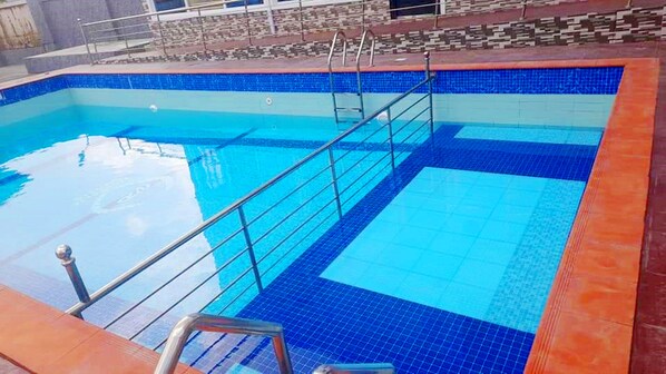 Una piscina con azulejos azules y una escalera metálica.