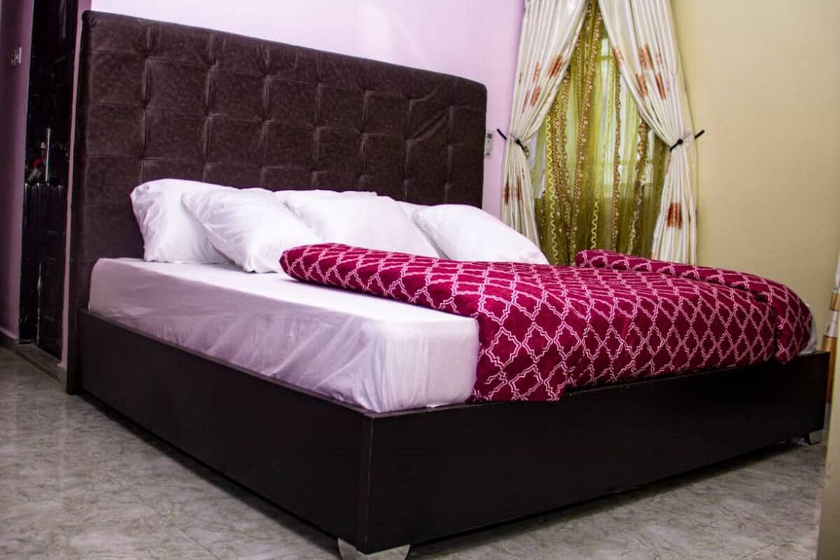 A bed with a dark headboard, white pillows, and a patterned red blanket.